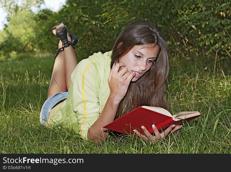 Beautiful girl reading a book while lying in the grass. Beautiful girl reading a book while lying in the grass