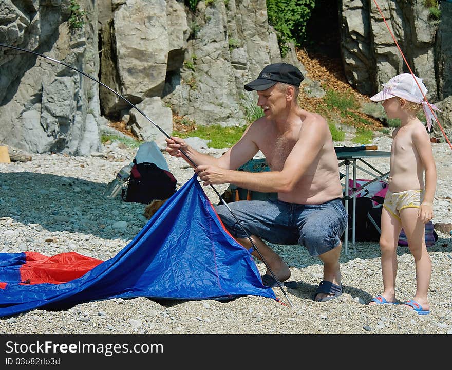 Father and daughter put a tent next to the rocks