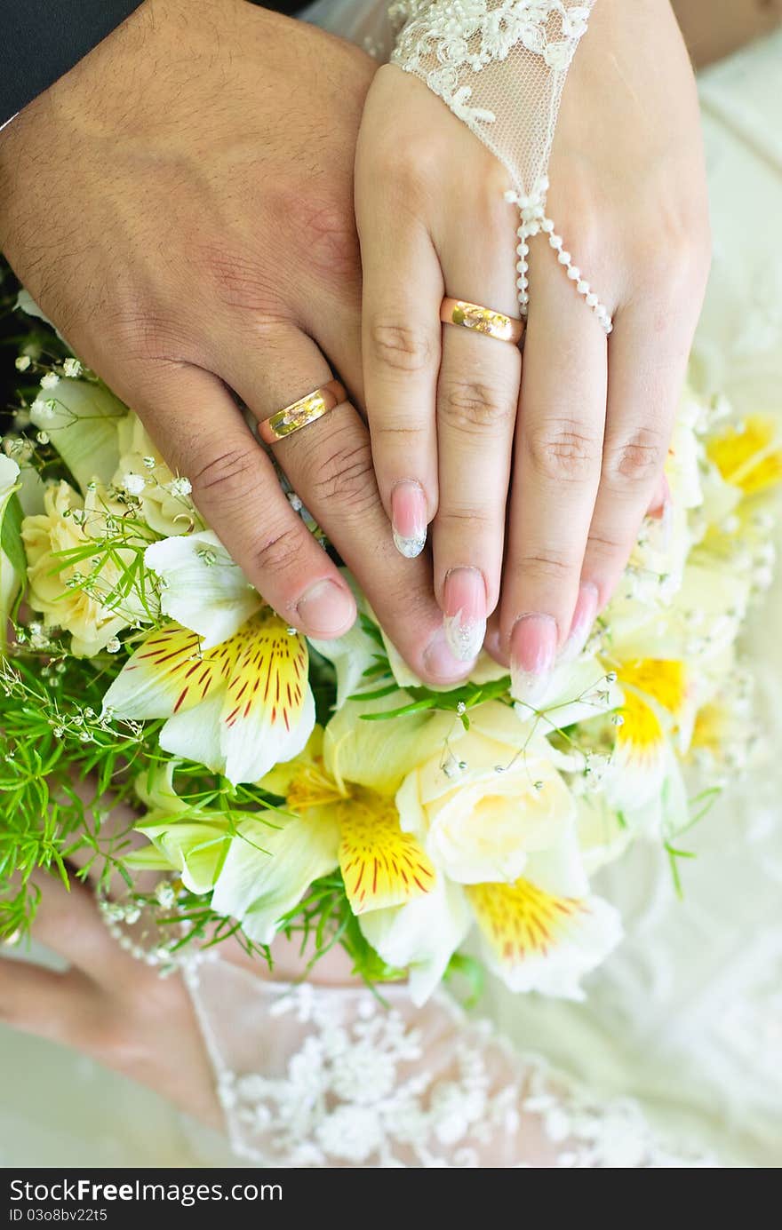 Hands of bride and groom with wedding rings over the bridal bouquet. Hands of bride and groom with wedding rings over the bridal bouquet