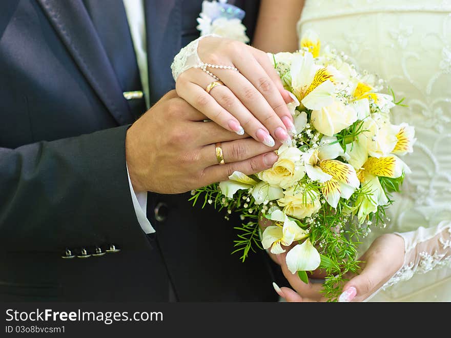 Hands of bride and groom with wedding rings over the bridal bouquet. Hands of bride and groom with wedding rings over the bridal bouquet