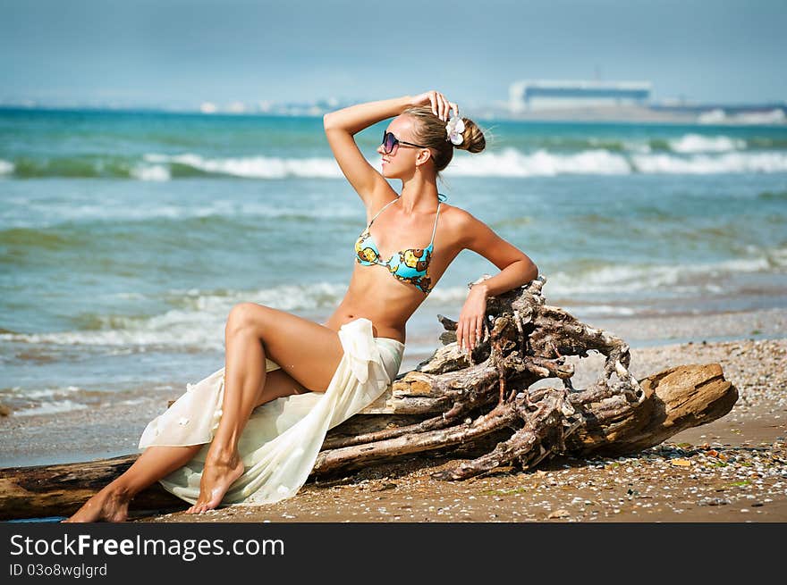 Young woman sitting on the log on the beach