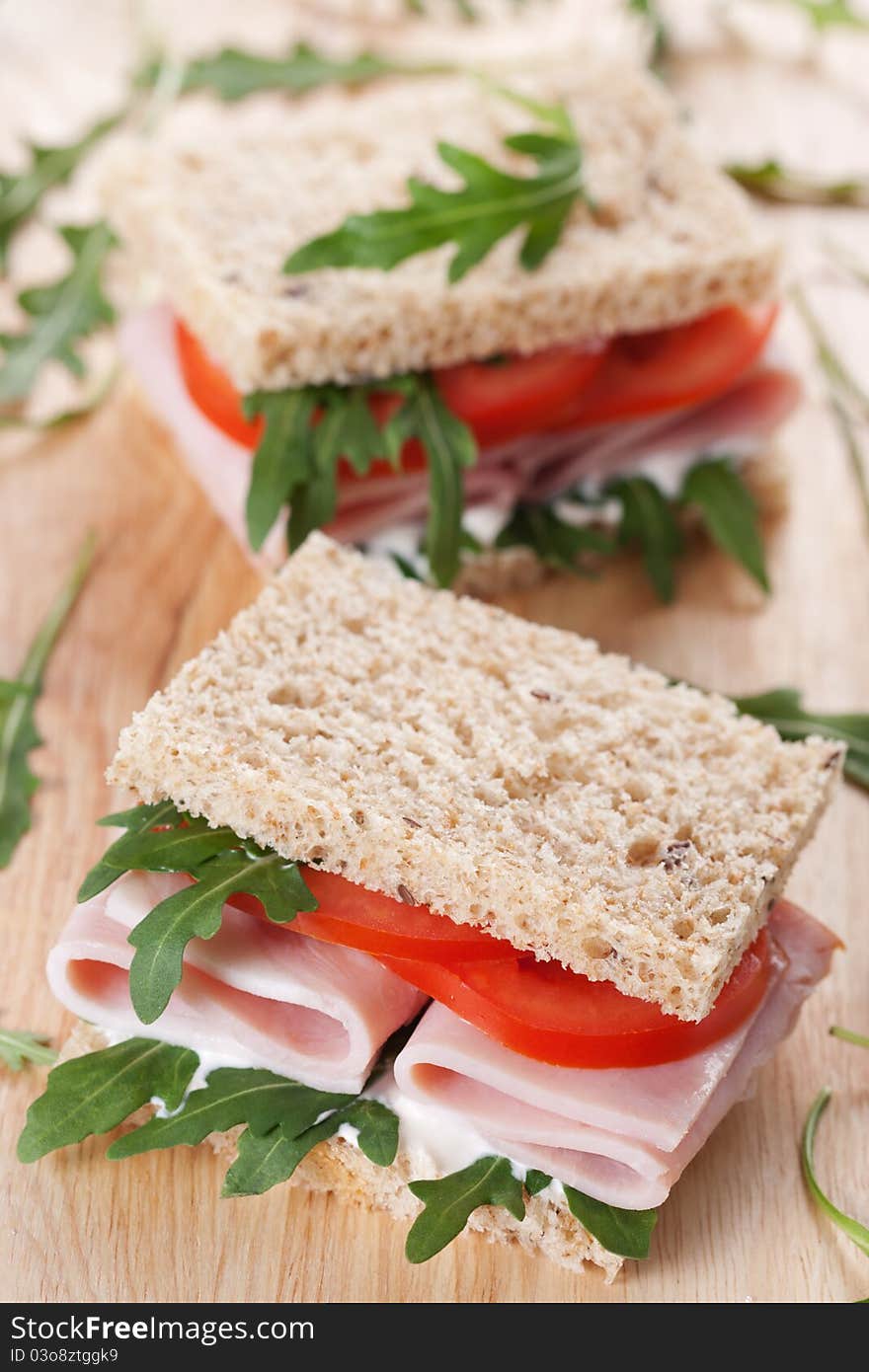 Sandwich with ham,tomato, and rucola salad on the wooden cutting board