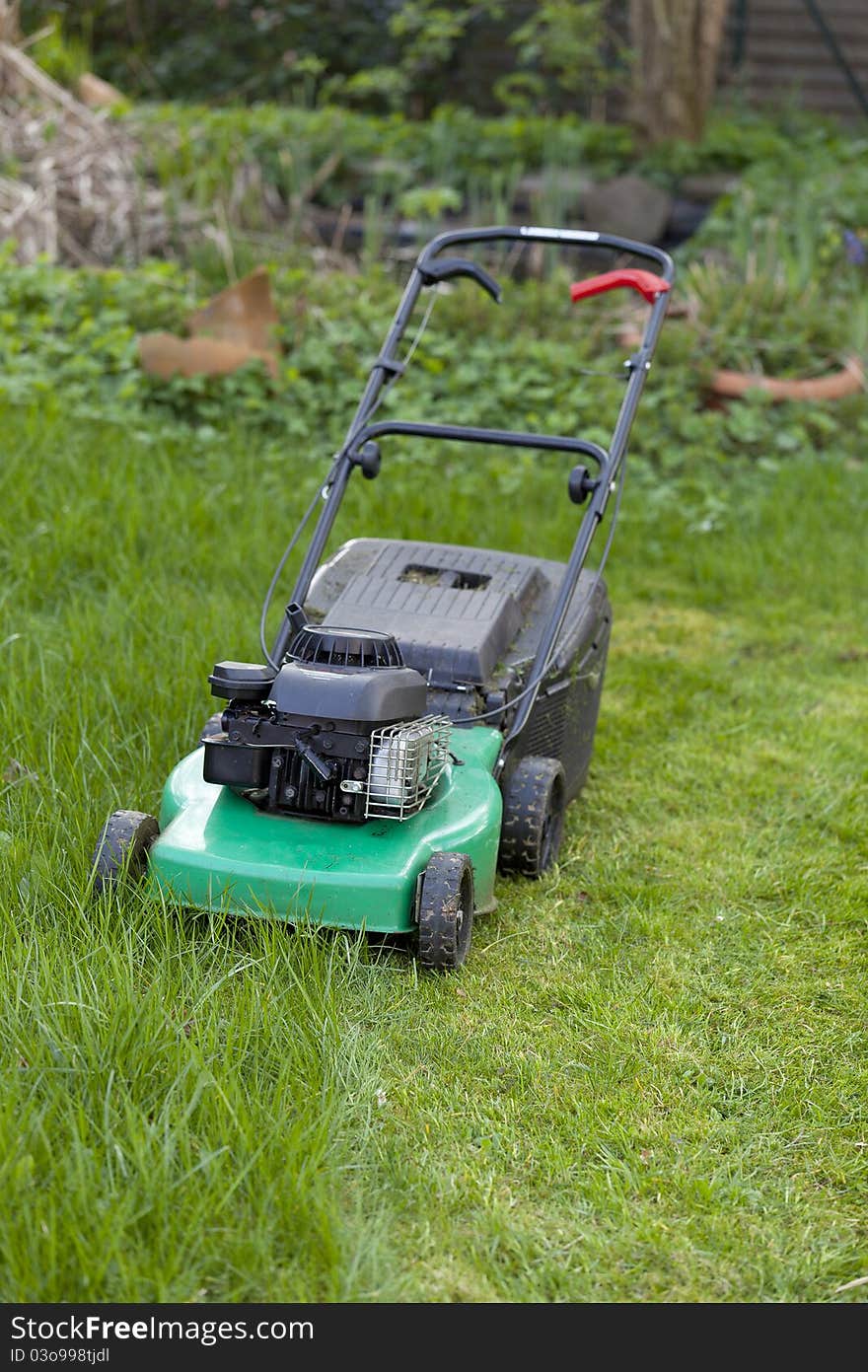 Lawnmower on half cutted green lawn.