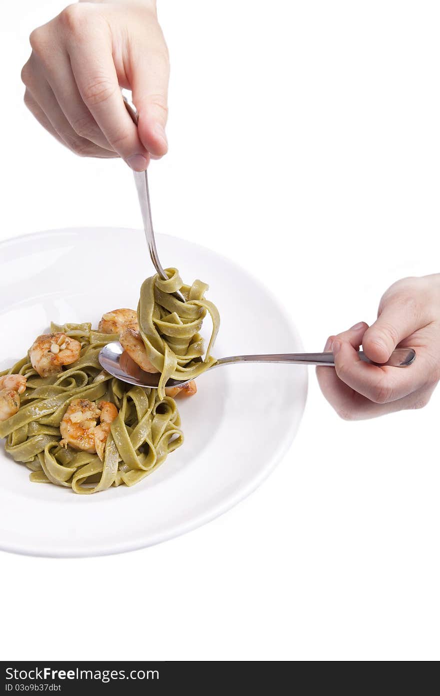 Hand holding fork and spoon for eating tagliatelle with shrimps,herbs and olive oil. tagliatelle swirled around a fork.