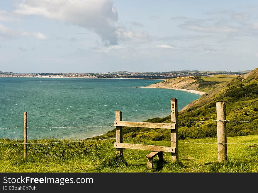 A wooden stile on the Dorset coast path with Weynmouth in the distance