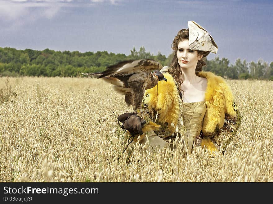 The woman in a beautiful old style dress with falcon has a rest before hunting in yellow field. The woman in a beautiful old style dress with falcon has a rest before hunting in yellow field.