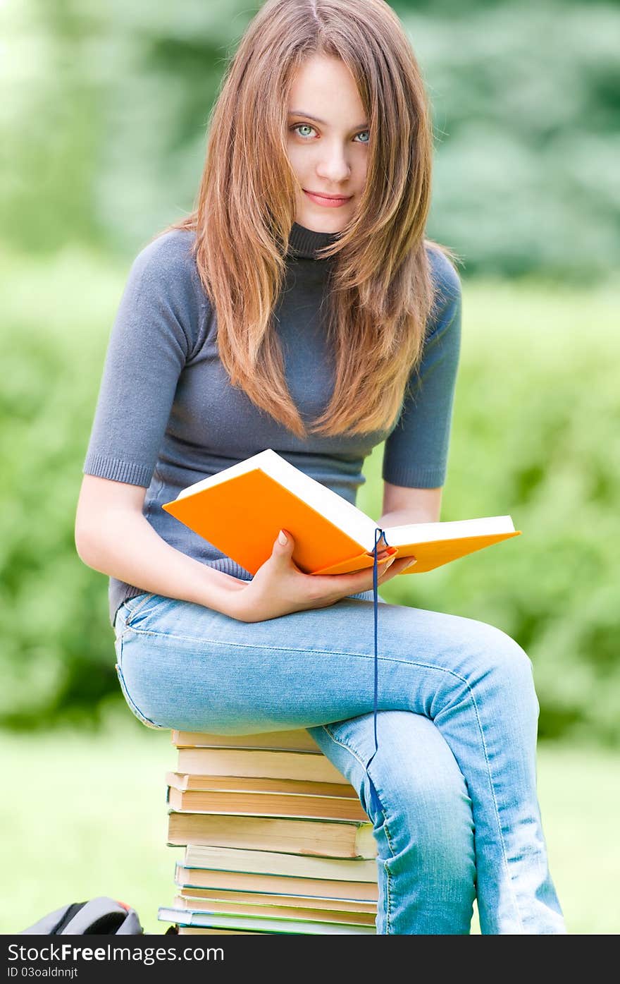 Happy student girl sitting on pile of books