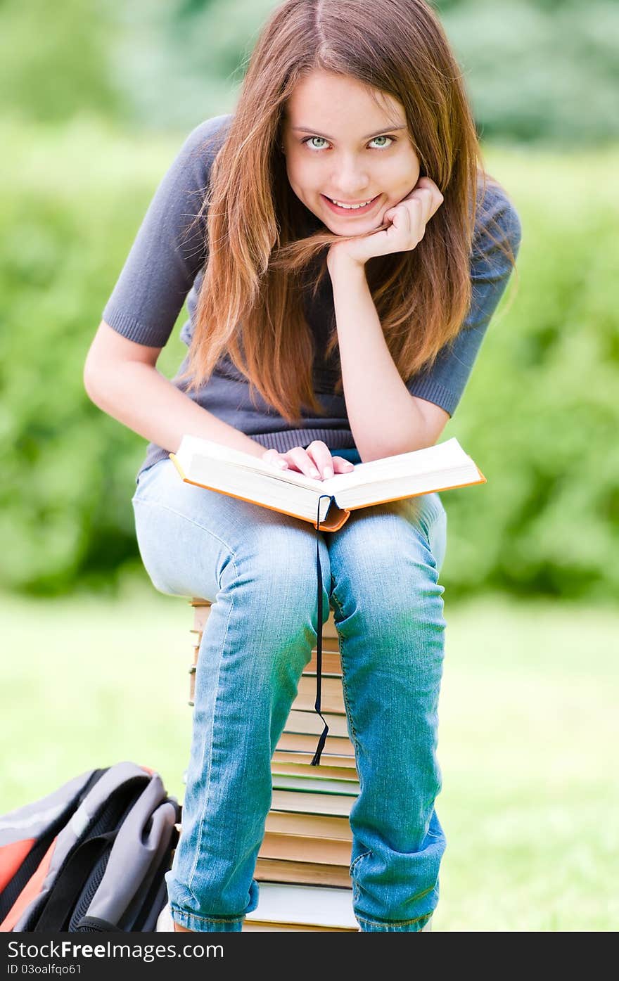 Happy student girl sitting on pile of books