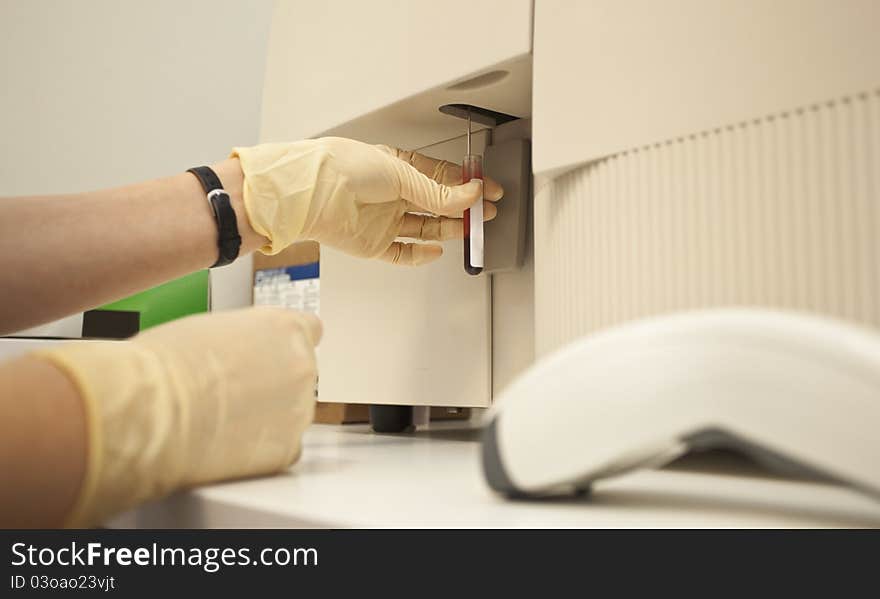 Close-up of hands with gloves holding a tube under blood analysis machine