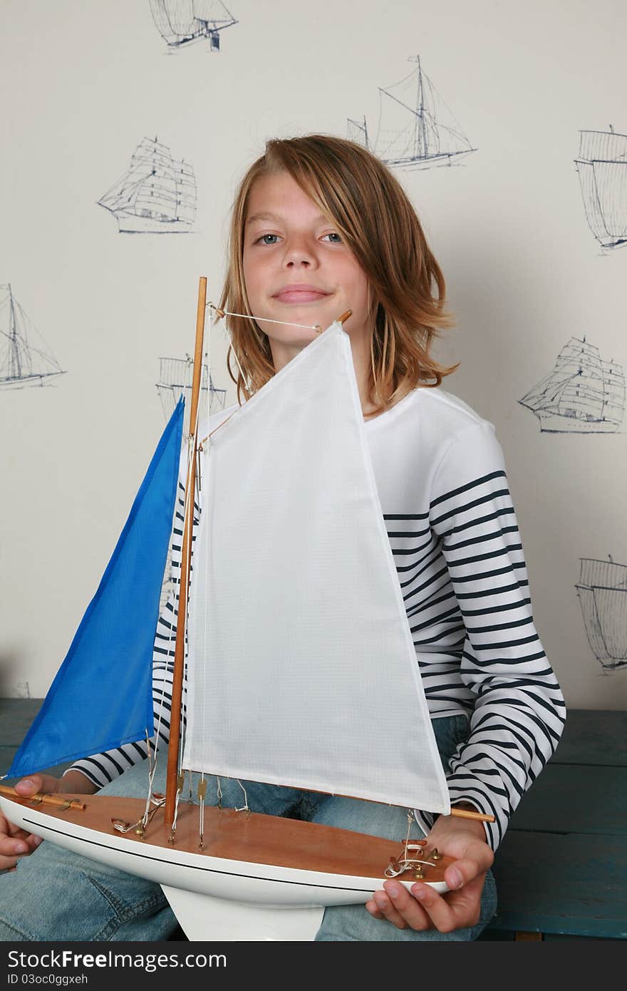 Young boy sitting on table holding toy sailboat on his hands. Young boy sitting on table holding toy sailboat on his hands