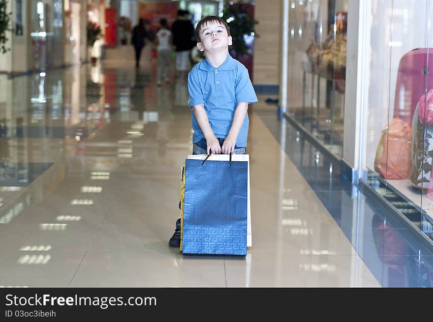 The child bears packages with purchases in shopping center. The child bears packages with purchases in shopping center