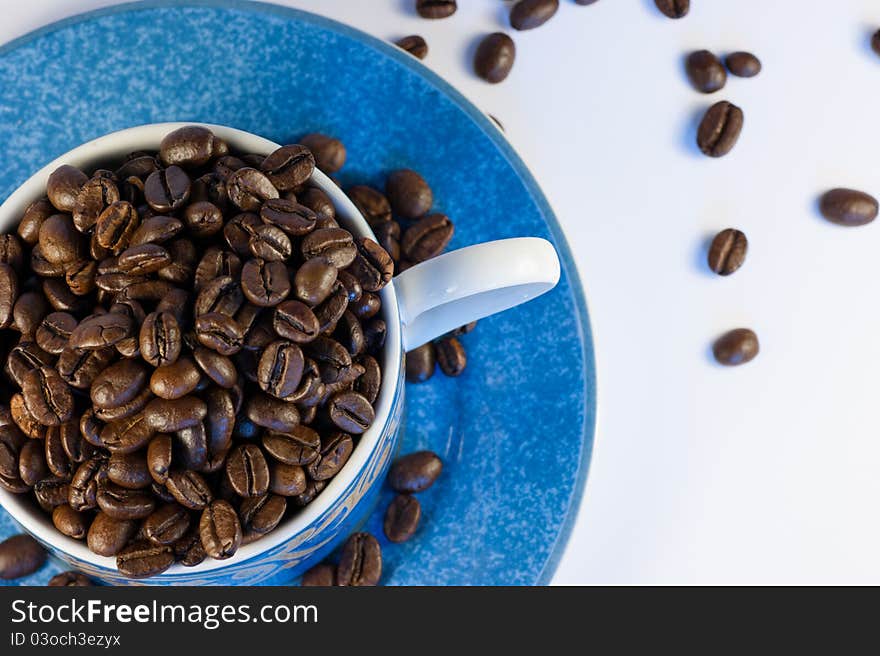 Dark roasted coffee beans in a cup and saucer. Dark roasted coffee beans in a cup and saucer