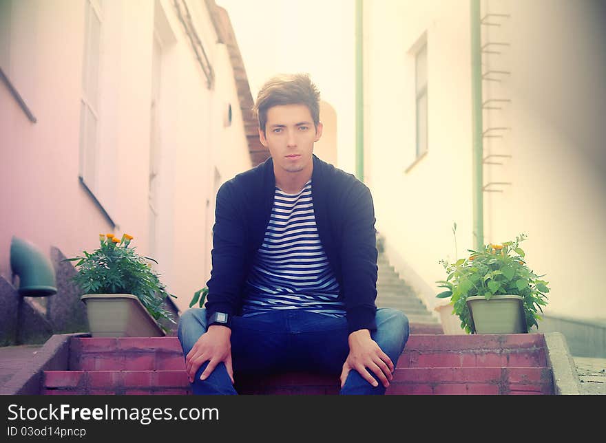 Young handsome man sitting on the stairs in the yard. Young handsome man sitting on the stairs in the yard