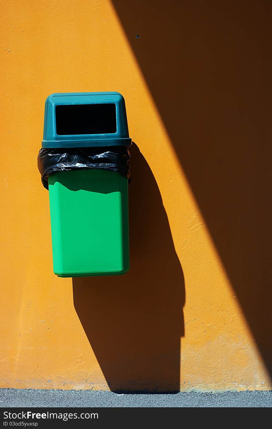 Green bin in the steet, orange wall with strong shadows