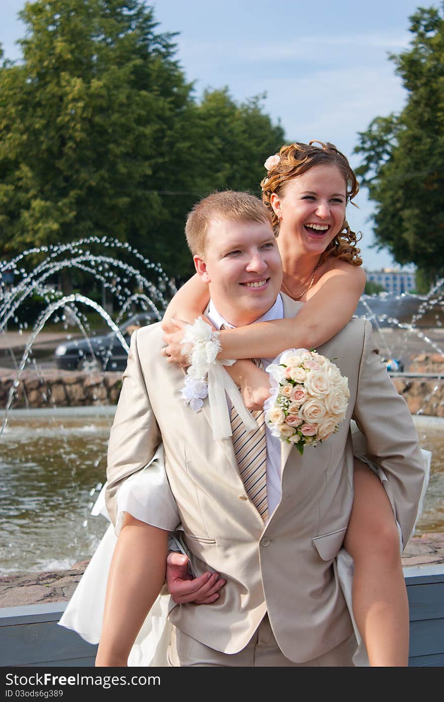 The bride sits on a back at the cheerful groom and laughs. The bride sits on a back at the cheerful groom and laughs