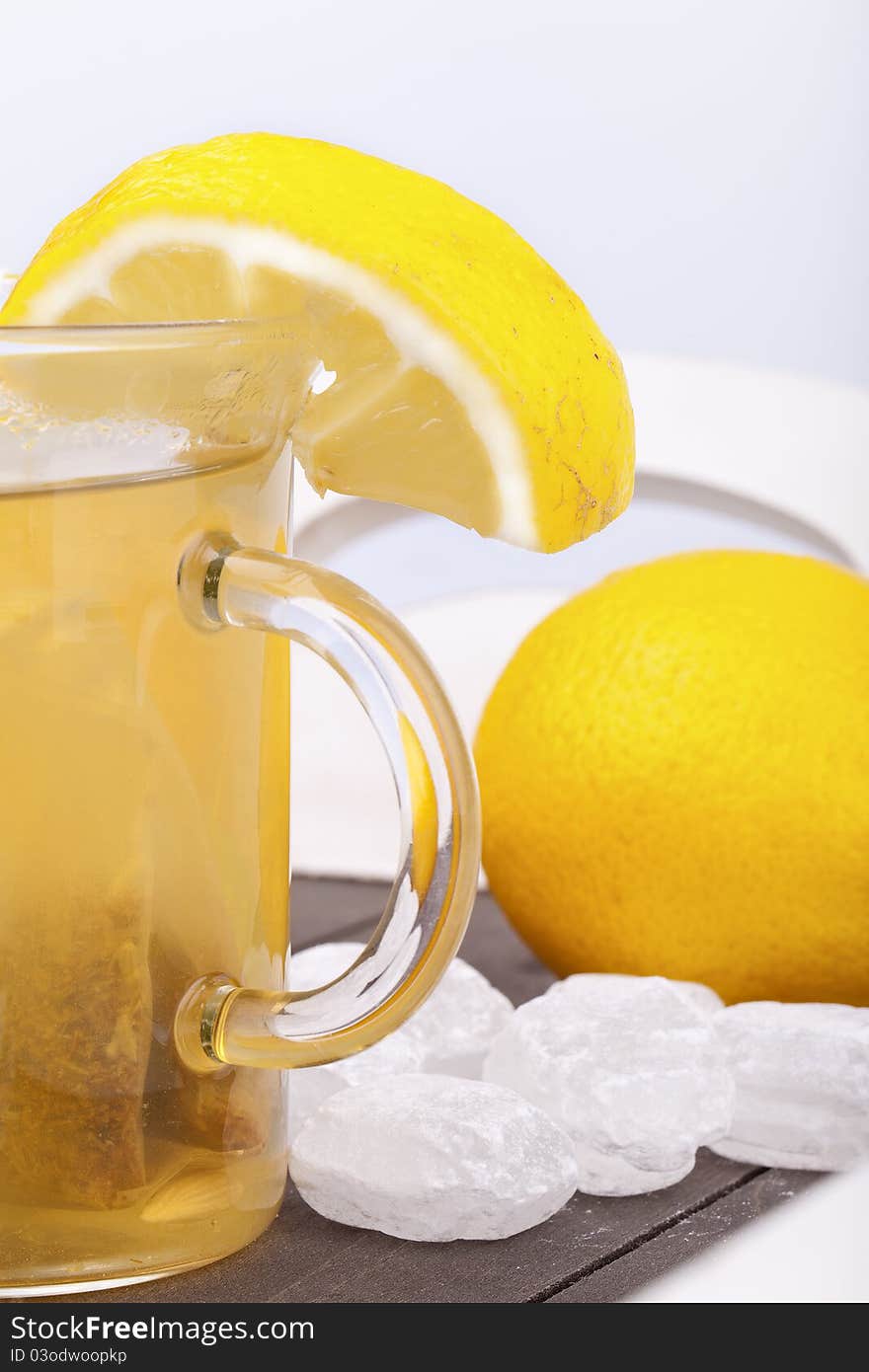 Studio-shot of a glass with hot lemon tea, a slice of lemon and rock sugar, on a wooden tray.