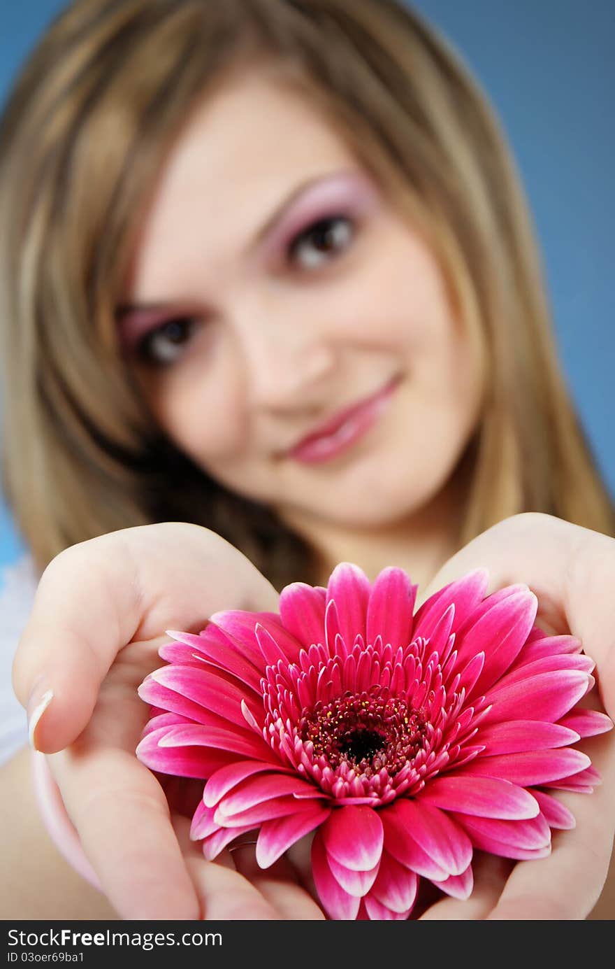 Attractive smiling woman portrait with flower in her hand on blue background