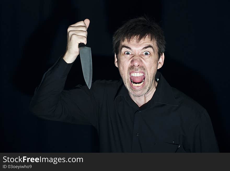 A crazy person with angry expression wielding a knife, on a black background. Low key lighting for dramatic effect. A crazy person with angry expression wielding a knife, on a black background. Low key lighting for dramatic effect.