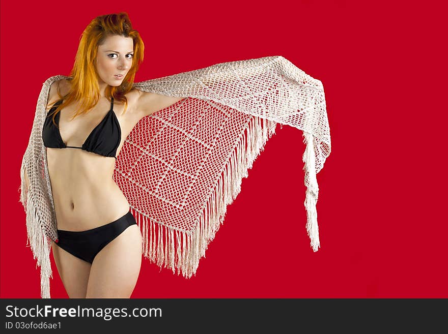 Red-haired young woman in a black bikini, with knitted scarf and a red background