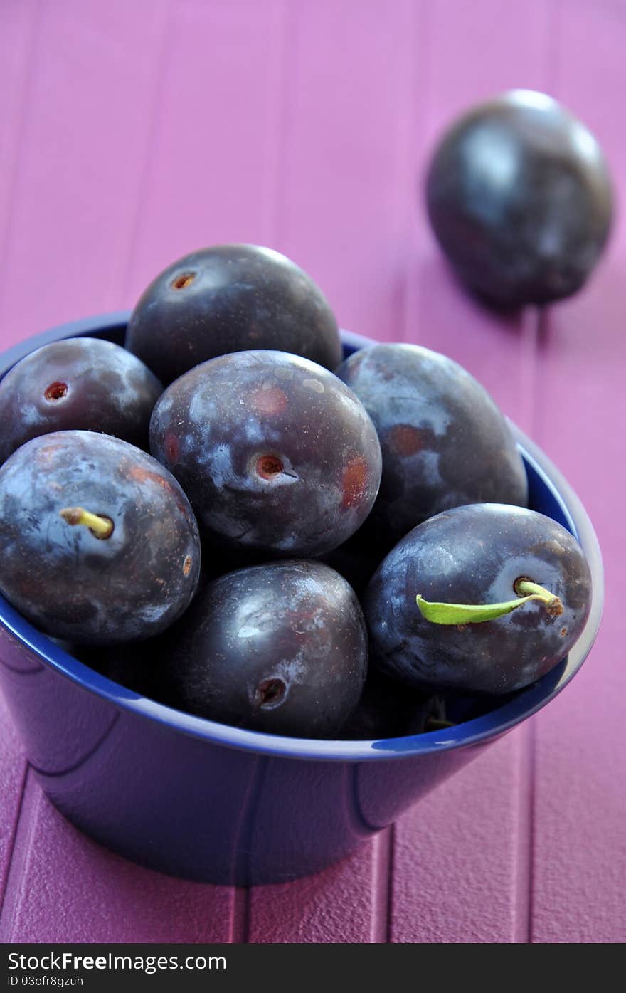 Fresh ripe plums in a navy blue bowl on purple background