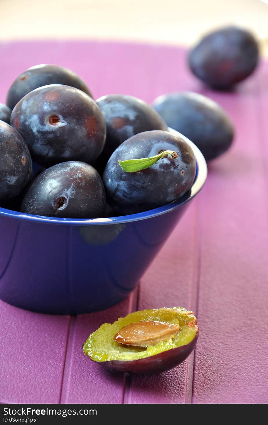 Fresh ripe plums in a navy blue bowl on purple background