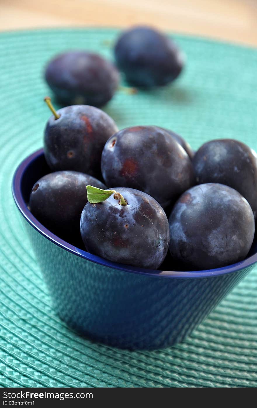 Fresh plums in a bowl in turquoise mat