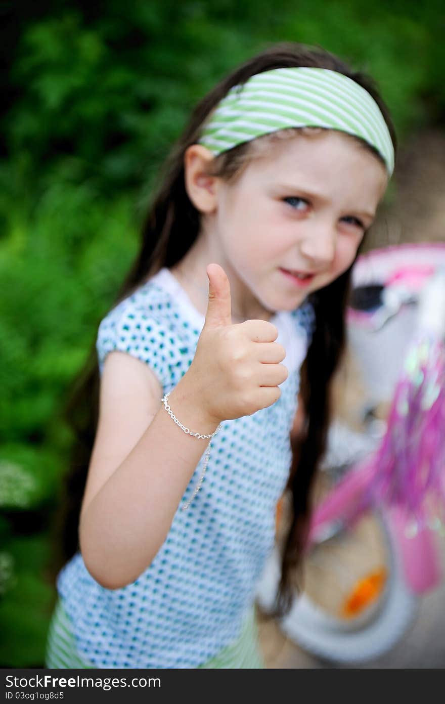 Beautiful long-haired child girl poses outdoors with thumbs up, focus on hand. Beautiful long-haired child girl poses outdoors with thumbs up, focus on hand