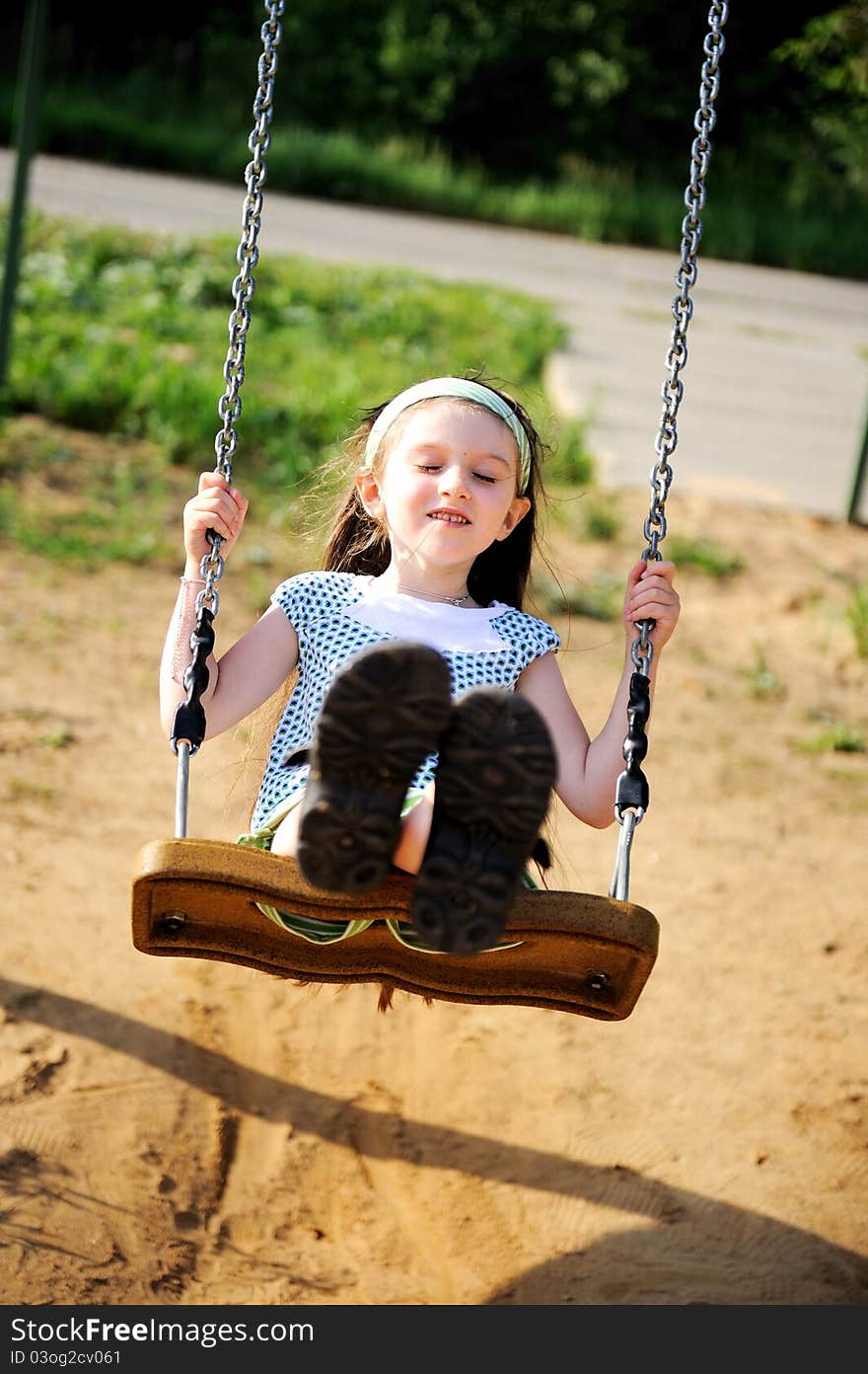 Happy child girl wearing green headband swings in the park. Happy child girl wearing green headband swings in the park