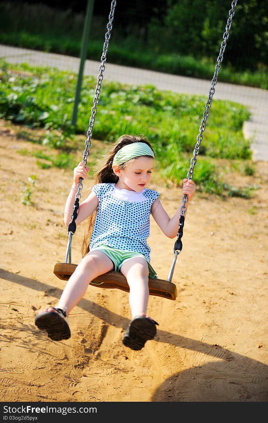 Happy child girl wearing green headband swings in the park. Happy child girl wearing green headband swings in the park