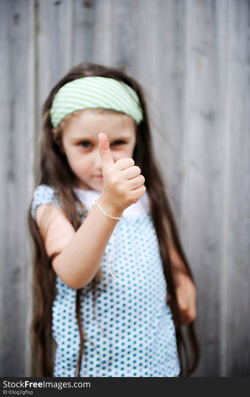 Beautiful long-haired child girl poses outdoors with thumbs up, focus on hand. Beautiful long-haired child girl poses outdoors with thumbs up, focus on hand