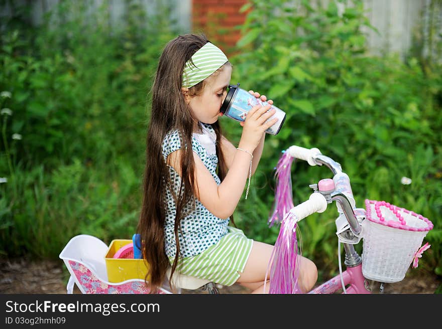 Adorable brunette child girl drinks while riding her pink bike. Adorable brunette child girl drinks while riding her pink bike