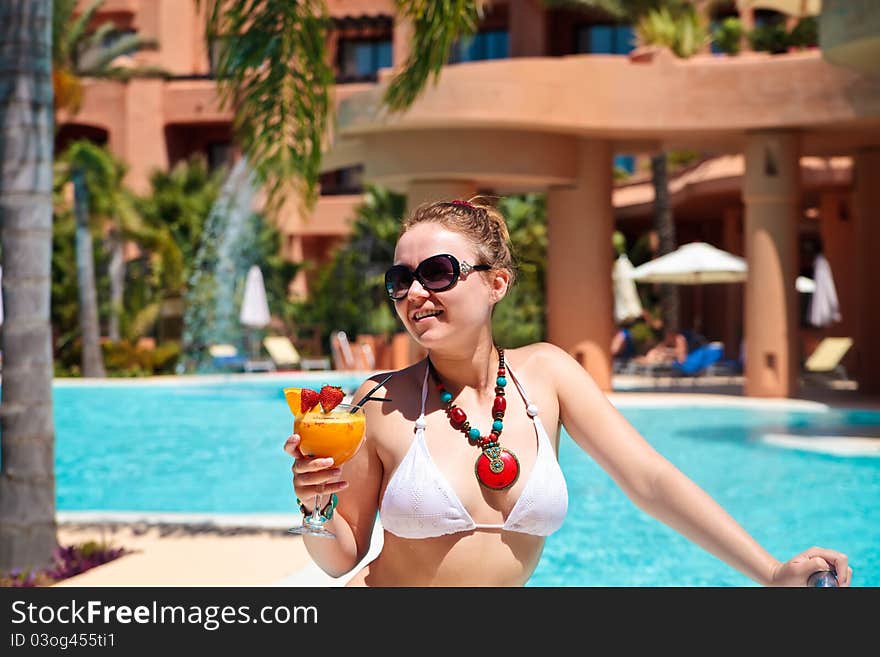 Beautiful young woman in bikini drinking cocktail with orange juice, standing in swimming pool, resort. Beautiful young woman in bikini drinking cocktail with orange juice, standing in swimming pool, resort