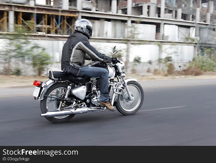 Motor biker breaks road rules by undertaking on the inside lane, horizontal landscape, copy space and crop space. Tarmac roads with white markings, derelict factory on roadside undergrowth. Motor biker breaks road rules by undertaking on the inside lane, horizontal landscape, copy space and crop space. Tarmac roads with white markings, derelict factory on roadside undergrowth