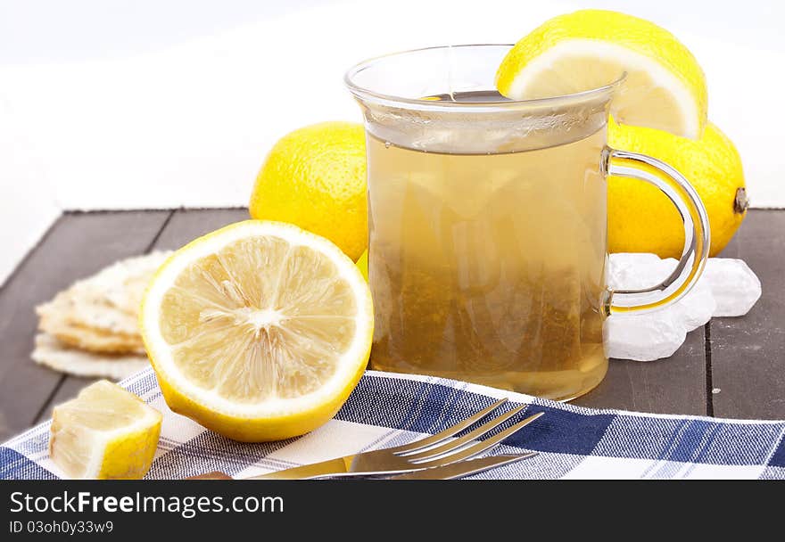 Studio-shot of a glass with hot lemon tea, a slice of lemon and rock sugar, on a wooden tray.