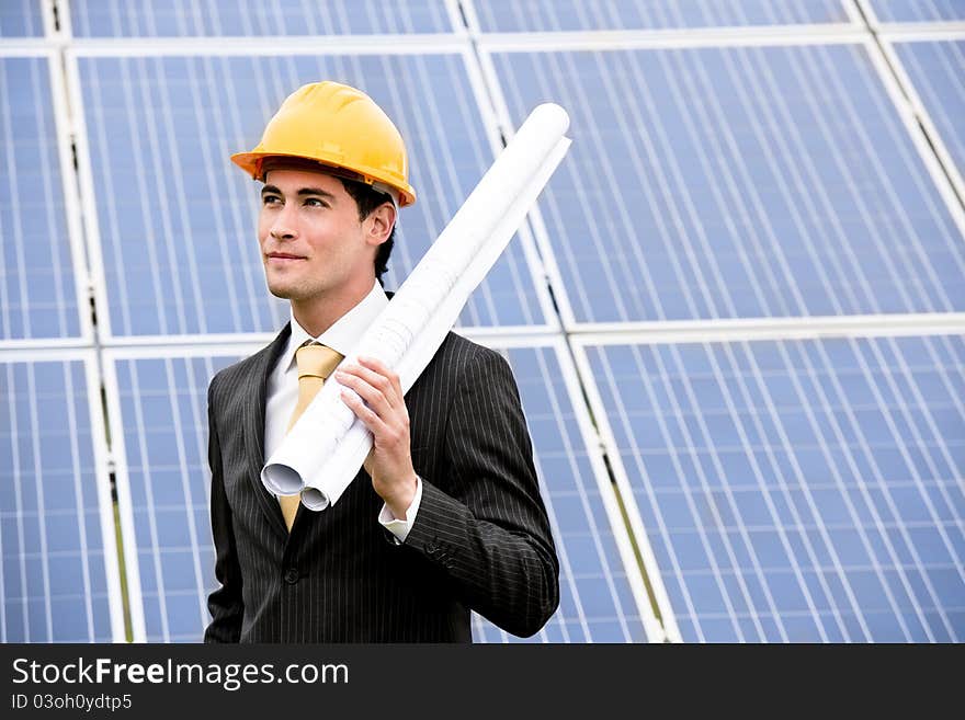 Male engineer at solar power station holding blueprints.