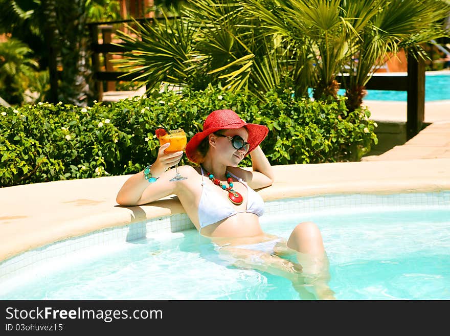 Beautiful woman in bikini and red hat siting in swimming pool with cocktail. Beautiful woman in bikini and red hat siting in swimming pool with cocktail