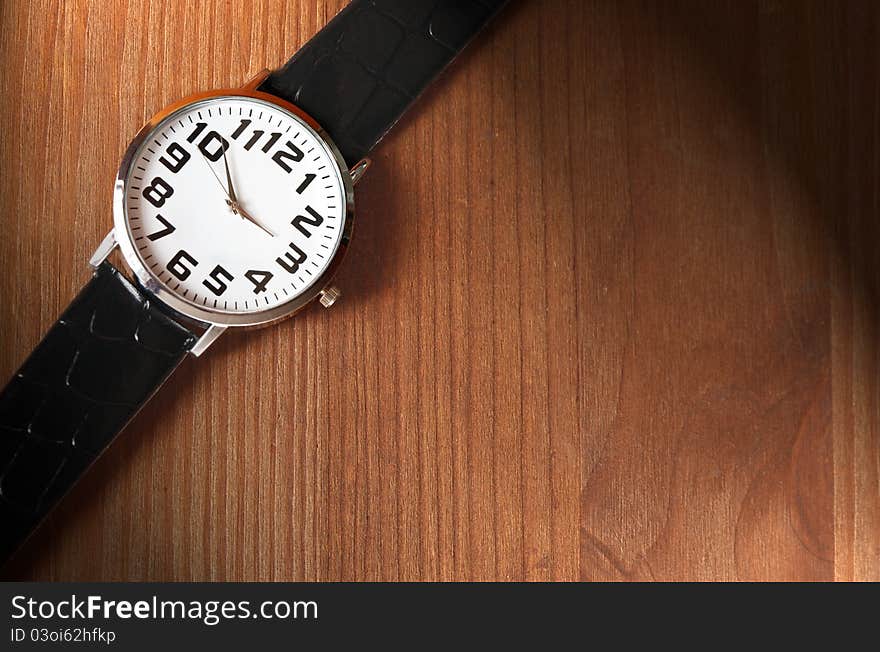 Modern wristwatch on wooden surface with lighting effect