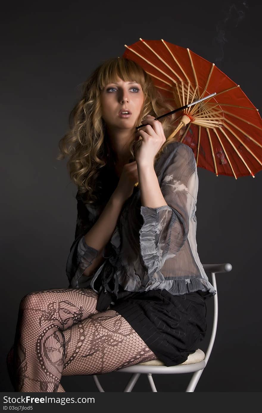 Portrait of the beautiful woman with long curly hair, smokes sitting on a chair