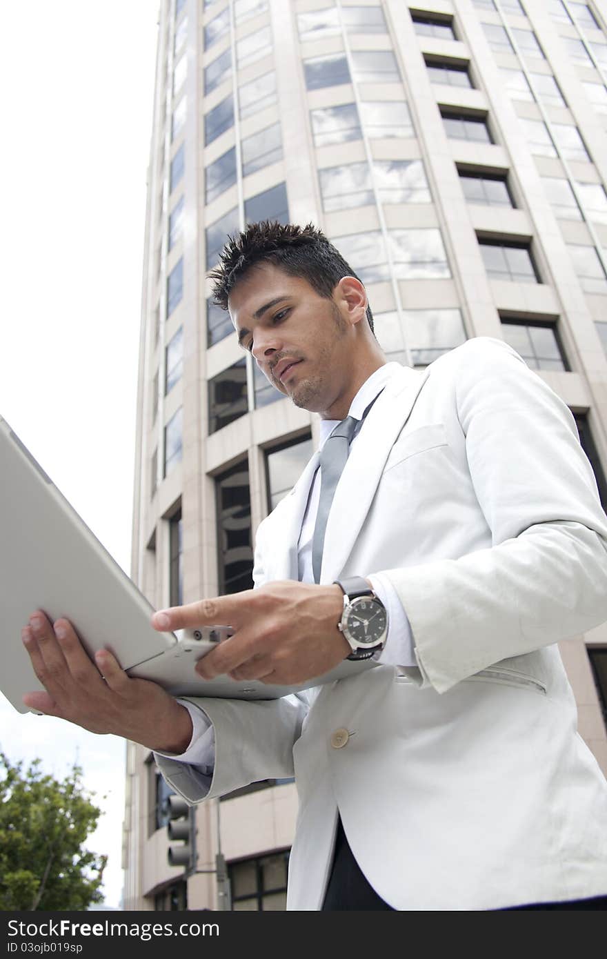 Busines man standing next to the office building and holding computer. Busines man standing next to the office building and holding computer