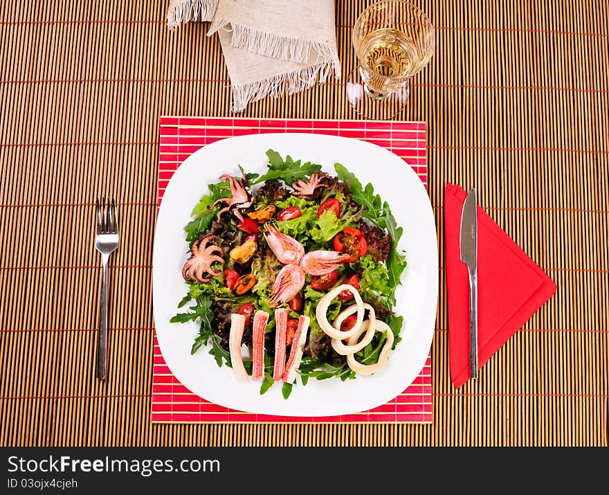 Italian fish salad on table with white wine glass, knife and fork