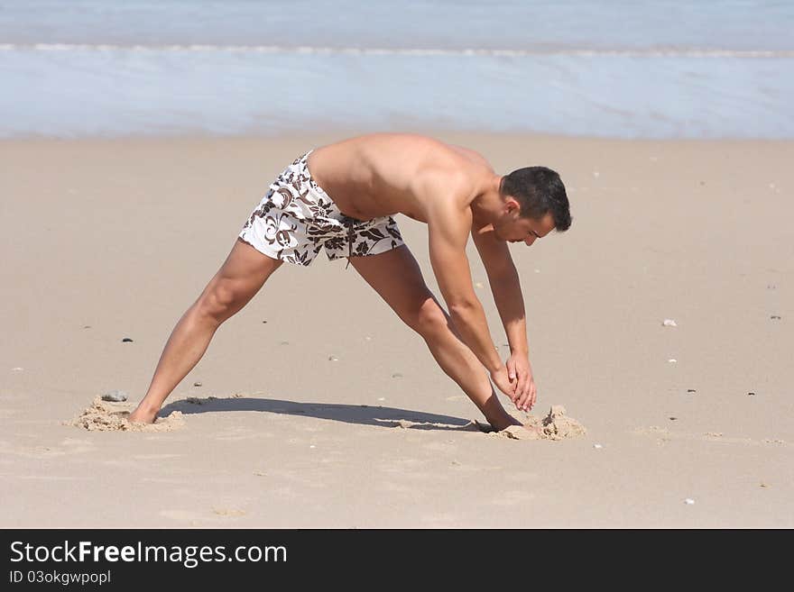 Attractive man making stretching movements before run on the beach