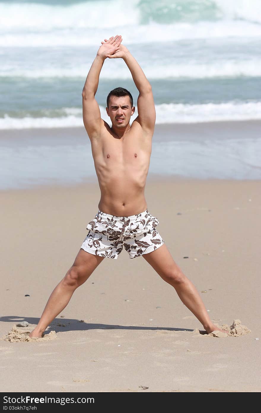 Attractive man making stretching movements before run on the beach