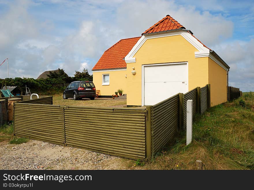 There are a modern house, a garage and a car in the yard against the sky. The yard is enclosed with fence. There are a modern house, a garage and a car in the yard against the sky. The yard is enclosed with fence.