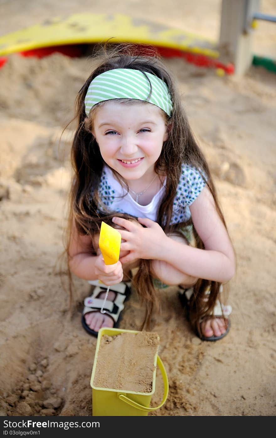 Happy child girl wearing green headband plays in a sandbox. Happy child girl wearing green headband plays in a sandbox