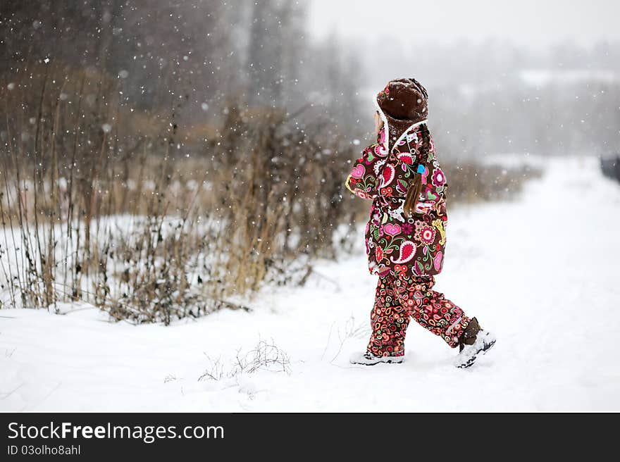 Child Girl In Colorful Snowsiut Plays In Snow