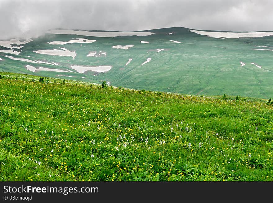 Summer landscape with green grass, mountains and clouds