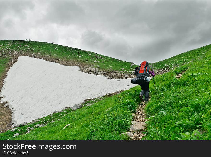 Tourist with a backpack walking along the road in the mountains. The mountains of North Caucasus.