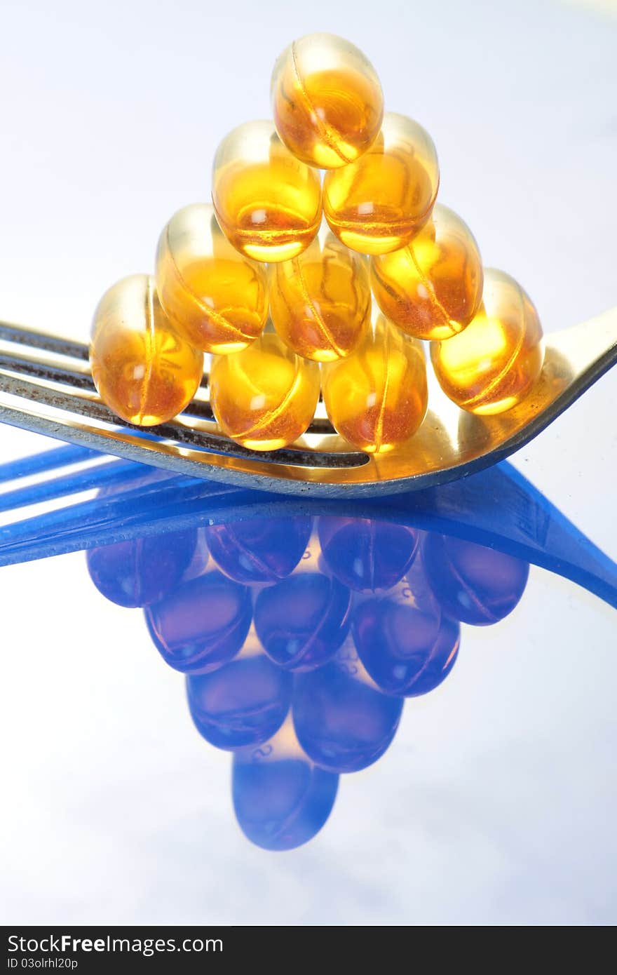 Fish oil pills arranged on a fork like a pyramid with a reflection below