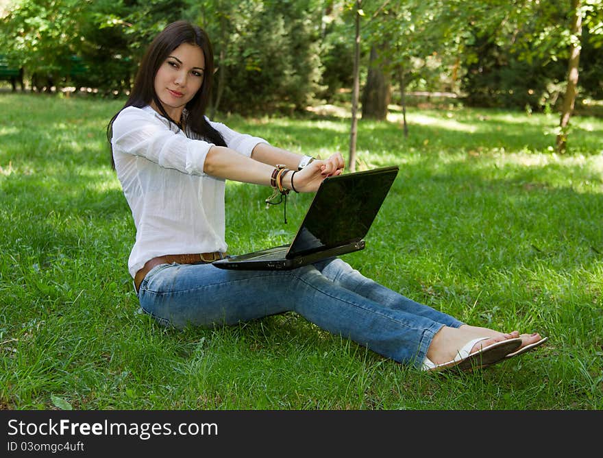 Beautiful woman with long hair wearing jeans stretched on the nature of the computer. Beautiful woman with long hair wearing jeans stretched on the nature of the computer