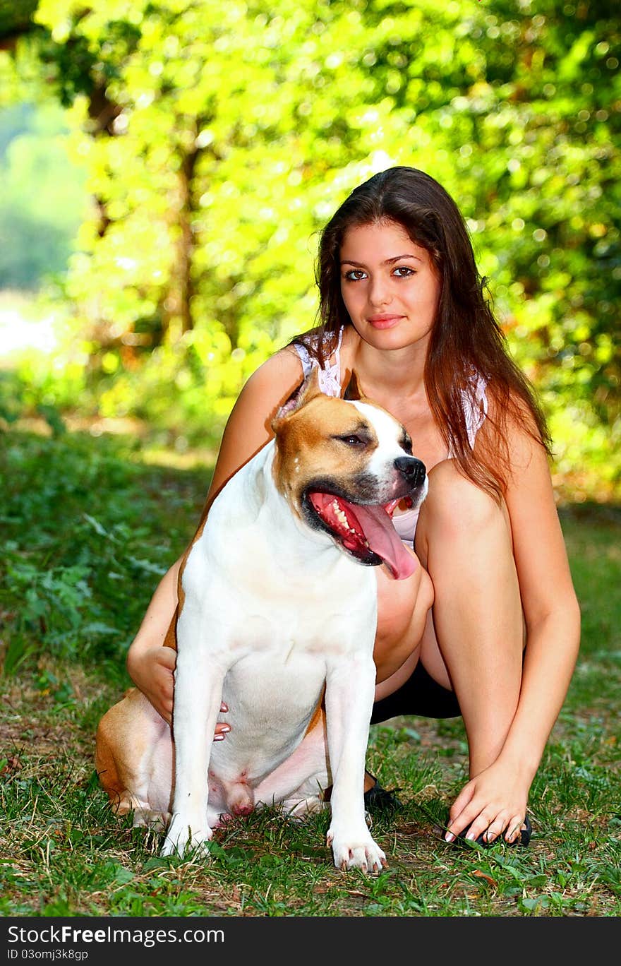 A vary beautiful girl hugging an American Staffordshire Terrier dog outside in a park meadow. A vary beautiful girl hugging an American Staffordshire Terrier dog outside in a park meadow